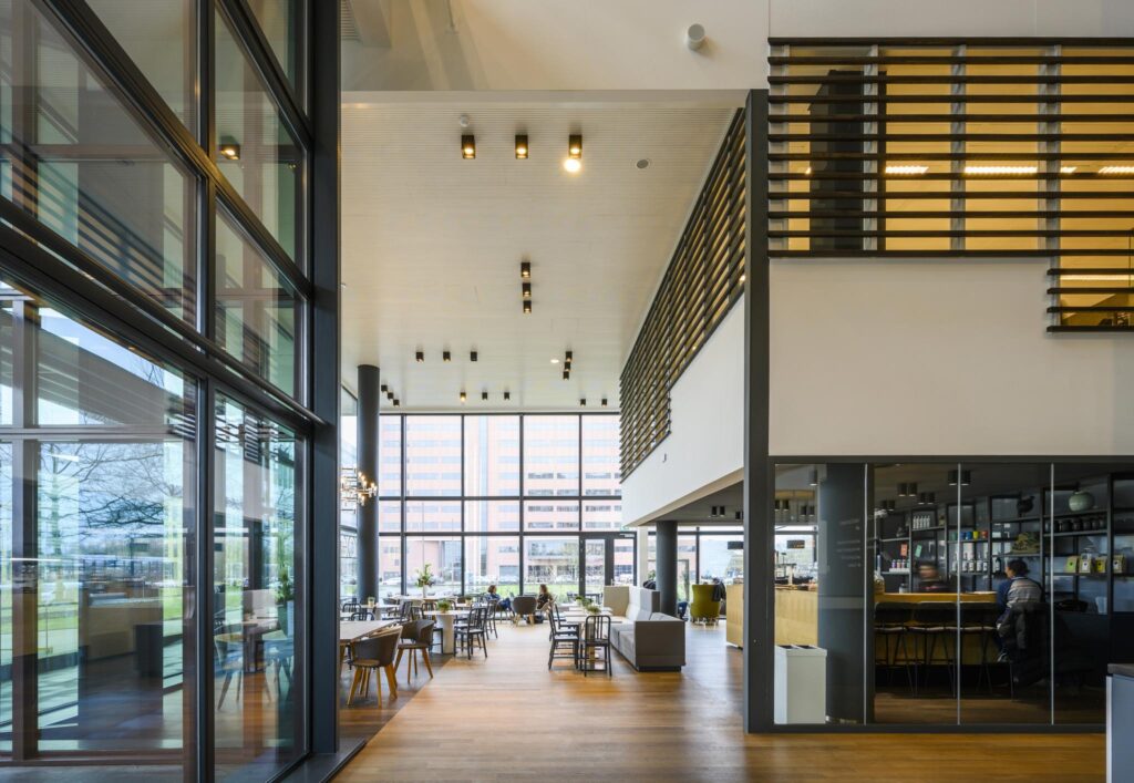 Moderne, open kantoorlobby aan de Thomas R. Malthusstraat met hoge plafonds, veel glas en een koffiebar.